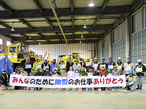 横断幕を掲げる園児と除雪作業者の集合写真
