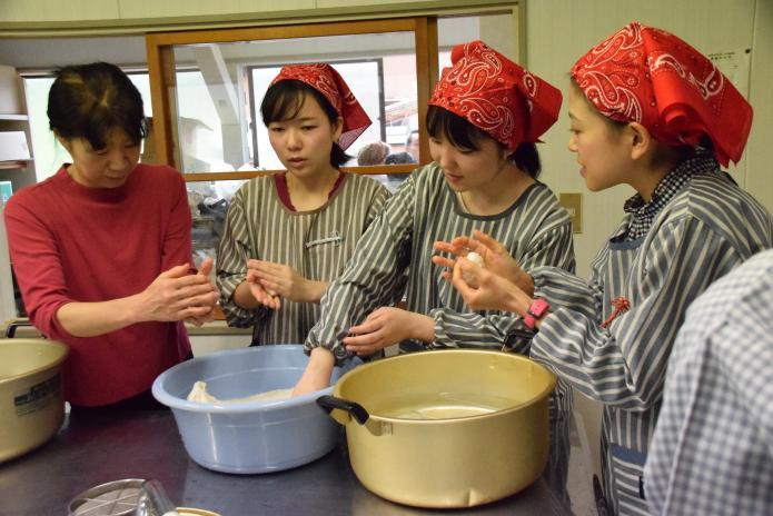 3人のインターン生と集落のお母さんが水を手に付けながらできたての餅をこねている写真