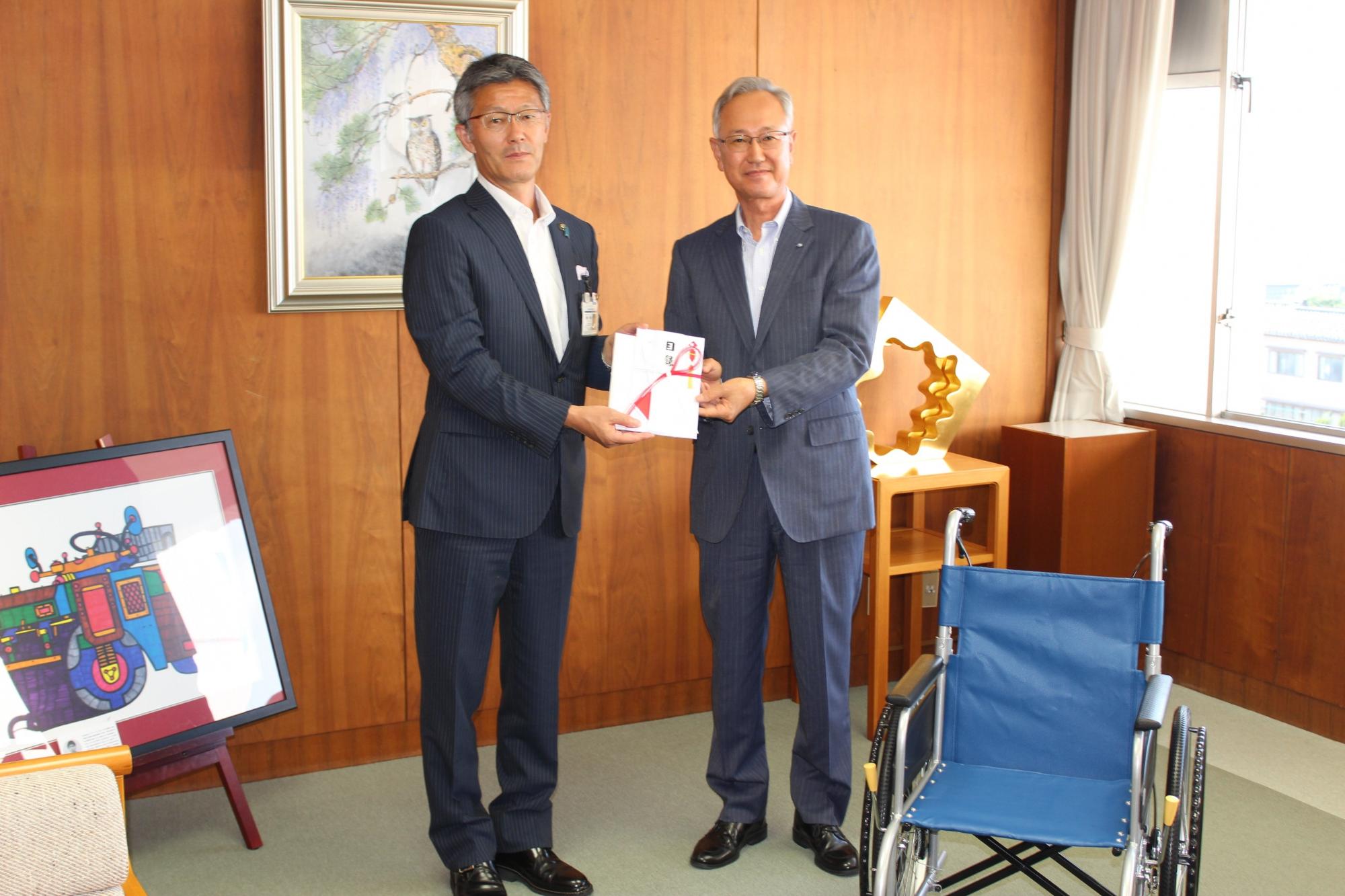 写真:柏崎信用金庫小出理事長から目録を手渡される櫻井市長。手前に寄付された車いすが写っています