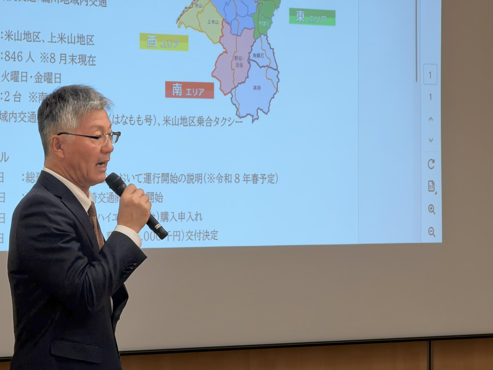 写真:マイクを持ち、スライドを使って市の施策を説明する市長