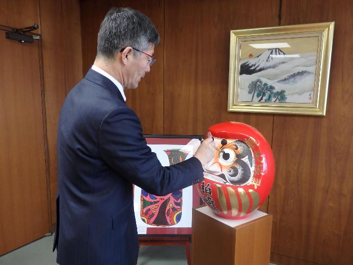 赤い大きなだるまの左目に筆で目を入れている櫻井市長