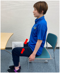 写真:椅子に腰かけ、太ももの間に挟んだ紙を落ちないように力を入れる女性