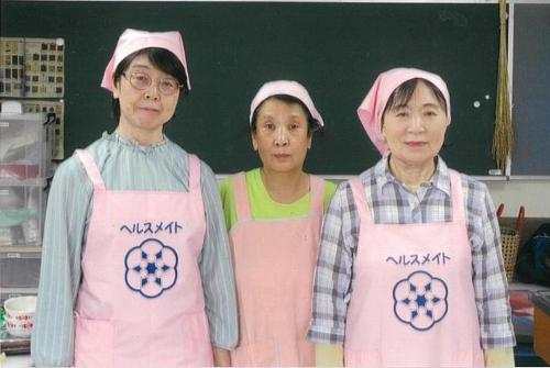 写真:ピンク色のエプロンと三角巾を身に着けた中通地区食生活改善推進員の3人の女性が写っています