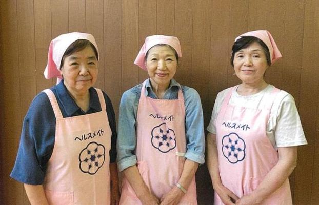 写真:ピンク色のエプロンと三角巾を身に着けた大洲地区と剣野地区食生活改善推進員の3人の女性が写っています