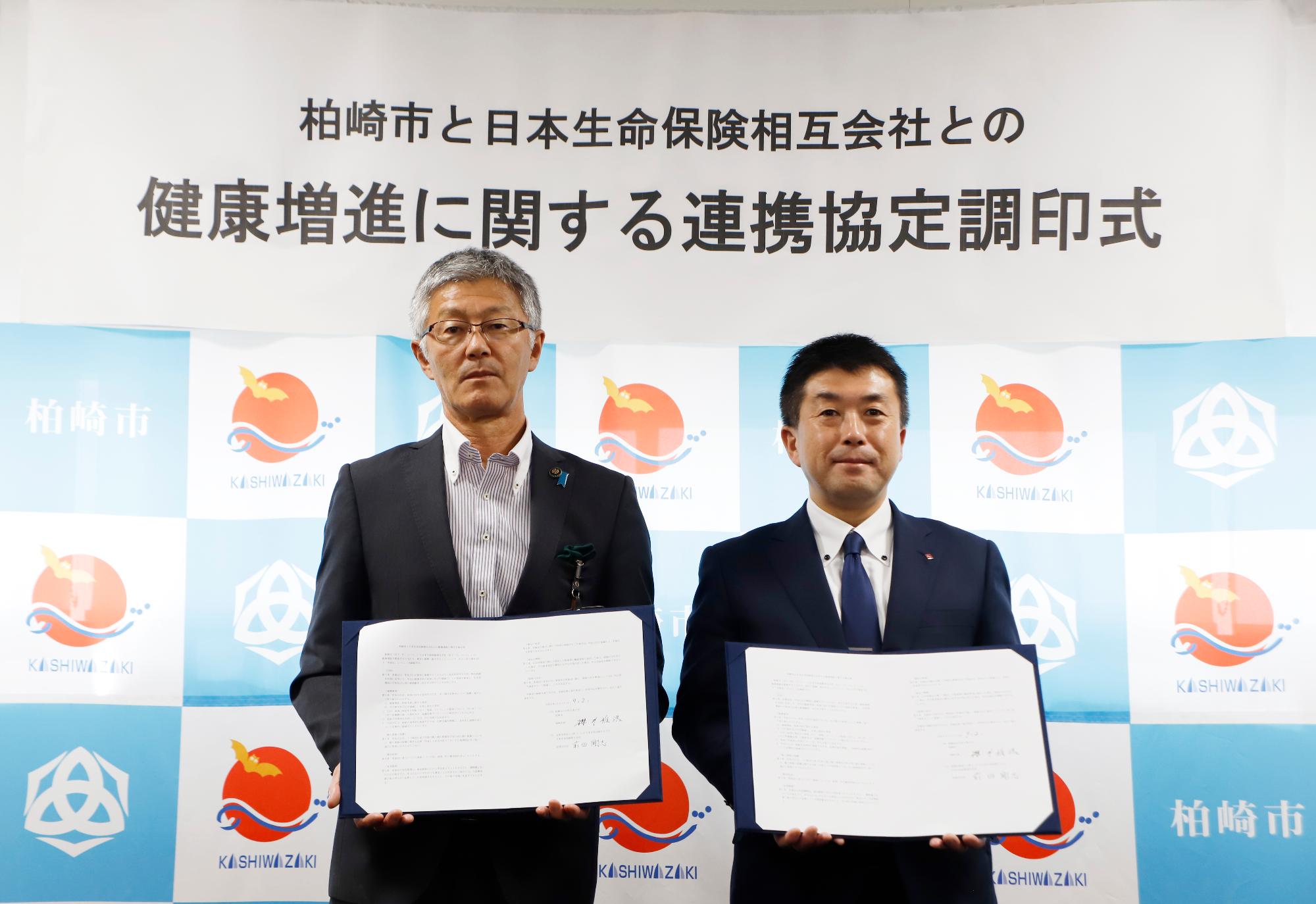 写真:桜井市長と日本生命保険相互会社関係者が並んで、取り交わした協定書を胸の前に掲げています。
