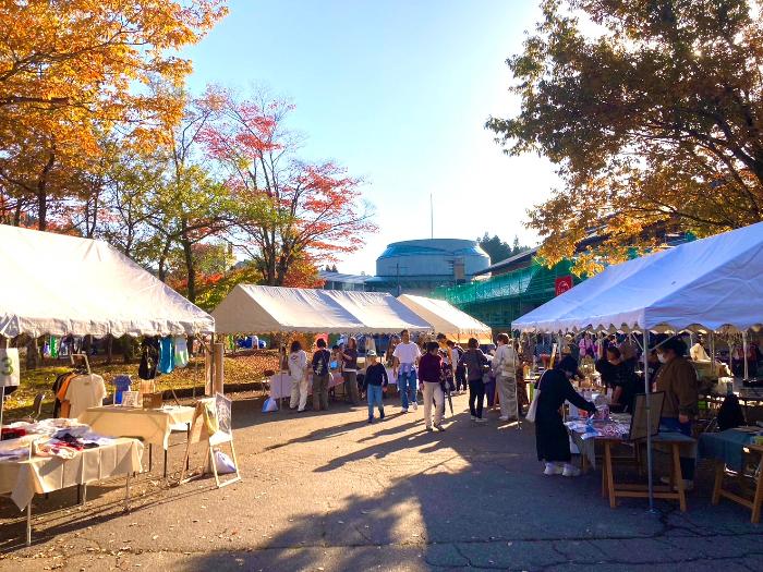 写真:秋晴れの空の下、フリーマーケットや飲食店のテントが立ち並ぶじょんのび村の広場