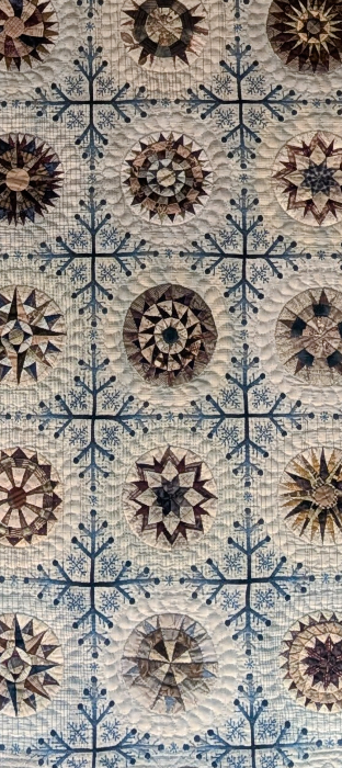 写真:白と青を背景に、さまざまな模様の花を布を縫い付けたキルト作品