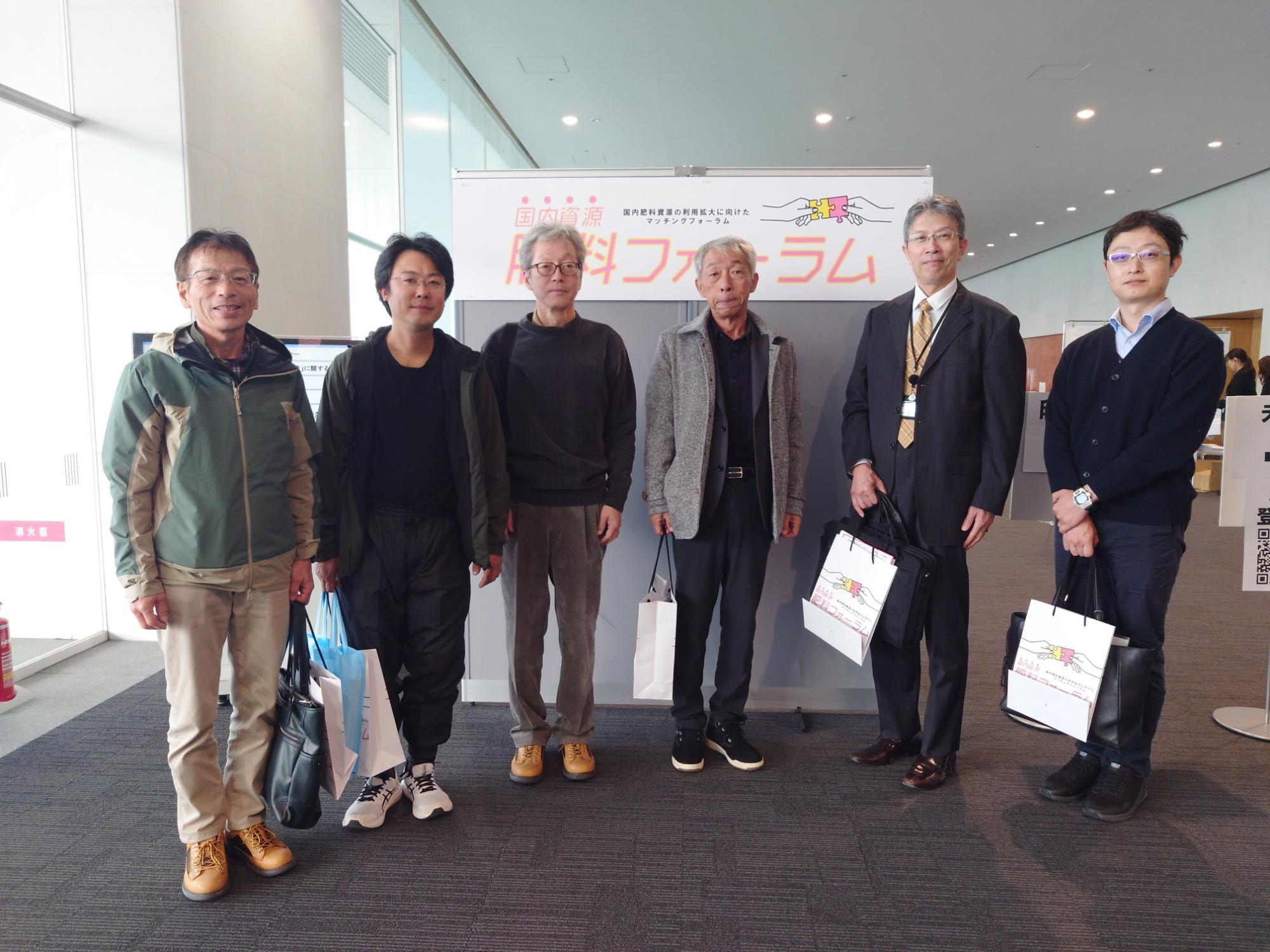 写真:参加者6人が会場入り口で笑顔で並んでいます