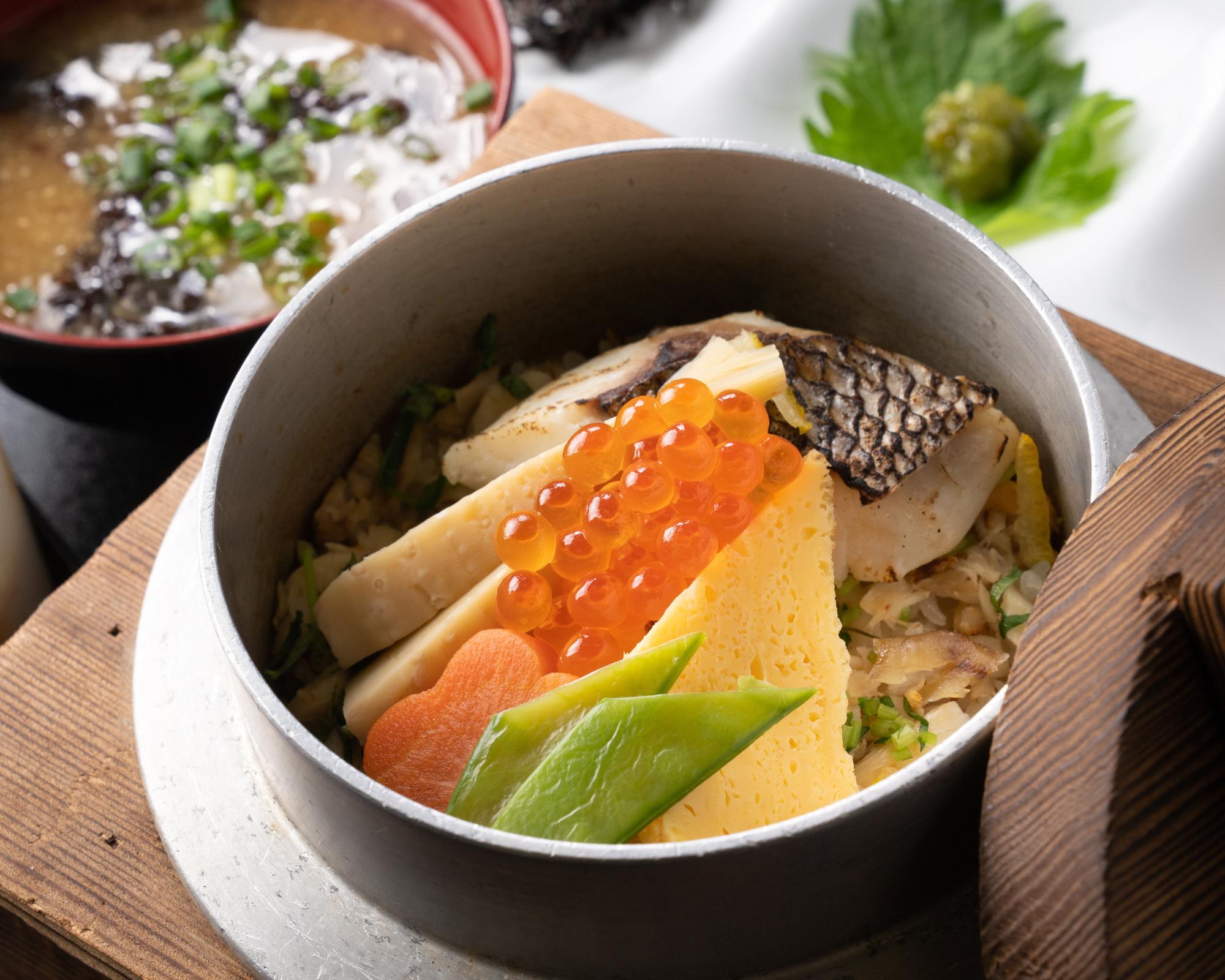写真:小さな釜に入った鯛めし。上には、焼き鯛、卵焼き、にんじん、いんげん、タケノコが盛り合わせてあり、一番上にイクラが飾り付けられています。