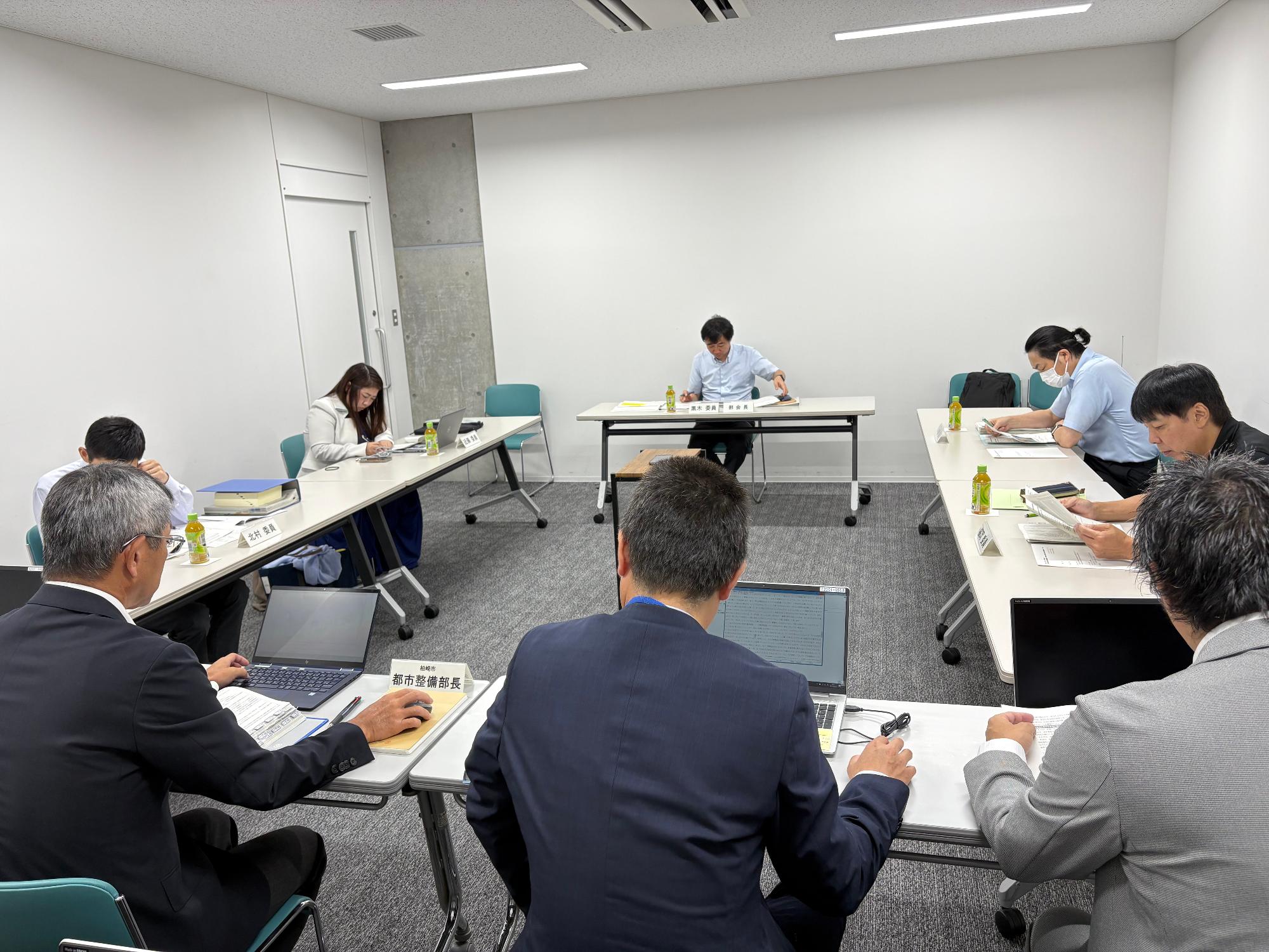 写真:第1回審議会の様子。市役所会議室で、委員と市職員が、報告・審議を行っています。