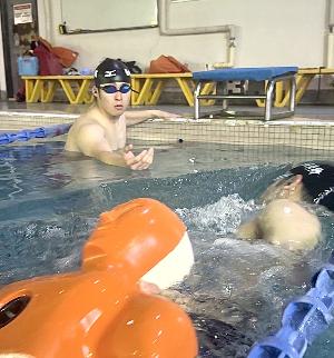 水中検索救助の写真。プールの中で1人が人形を仰向けにして及びながら運び、もう1人が引き受けるために待機しています。