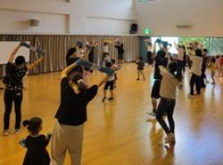 写真:PARTY体操の参加者が両手を頭の上にあげて両手でタオルを持ちながら音楽に合わせて体操をしている様子です