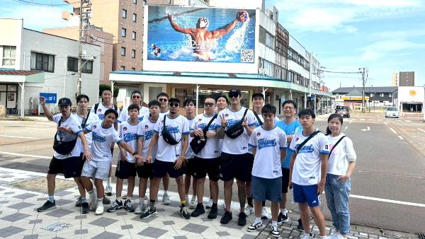 写真:駅前のアーケードの上にある巨大水球看板をバックに記念撮影