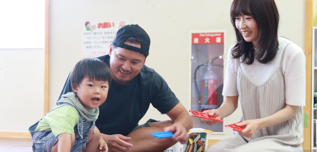 写真:電車のおもちゃで遊ぶはるく君ファミリー。左から順にはるく君、恭三さん、友美さんが写っています