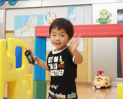 写真:車のおもちゃを手に持ち、笑顔で手を振る男の子