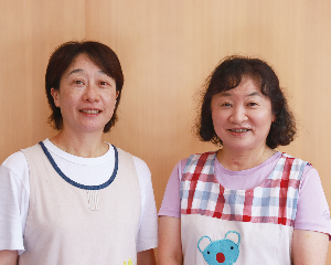 エプロンを付けた2人の女性保育士の写真があります