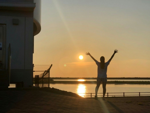 写真:日本海に沈む夕日に向かって大きく手を広げる後ろ姿の女性