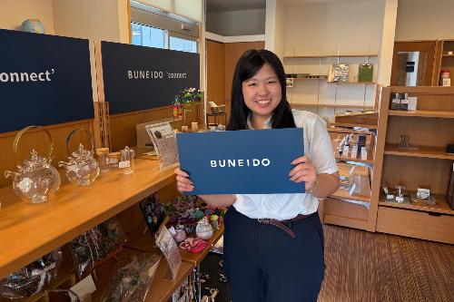 写真:小林文栄堂の店内で。おすすめ商品の棚の前で微笑む田川さん