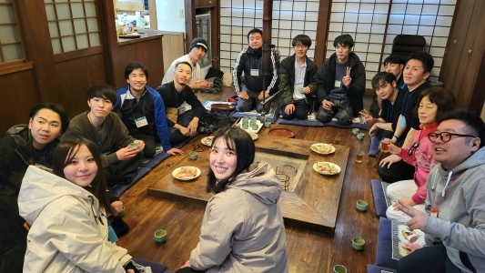 写真:地域での交流の様子。囲炉裏を囲んで、ボランティア参加者の若者が地域住民と話に花を咲かせています