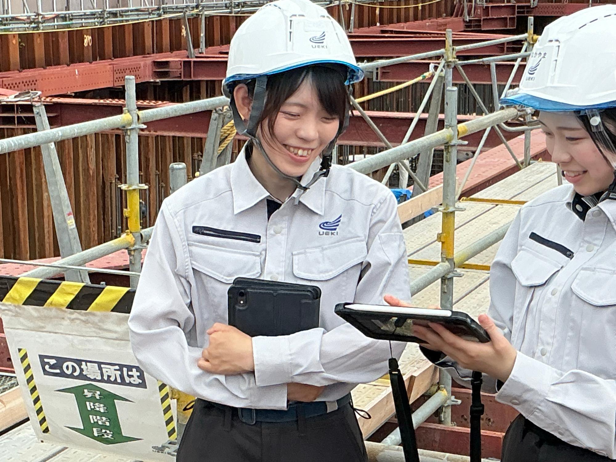 写真:工事現場の足場前でヘルメットをかぶり立って打り合わせをする橘さん