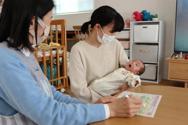 写真：助産師とお母さんが赤ちゃんを見て微笑んでいます