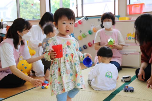 写真：子育て支援室で遊んでいる女の子がおもちゃのコップを持って見ています