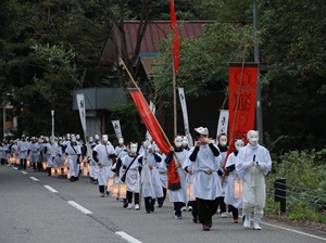 白い装束と狐のお面の人々の行列の写真