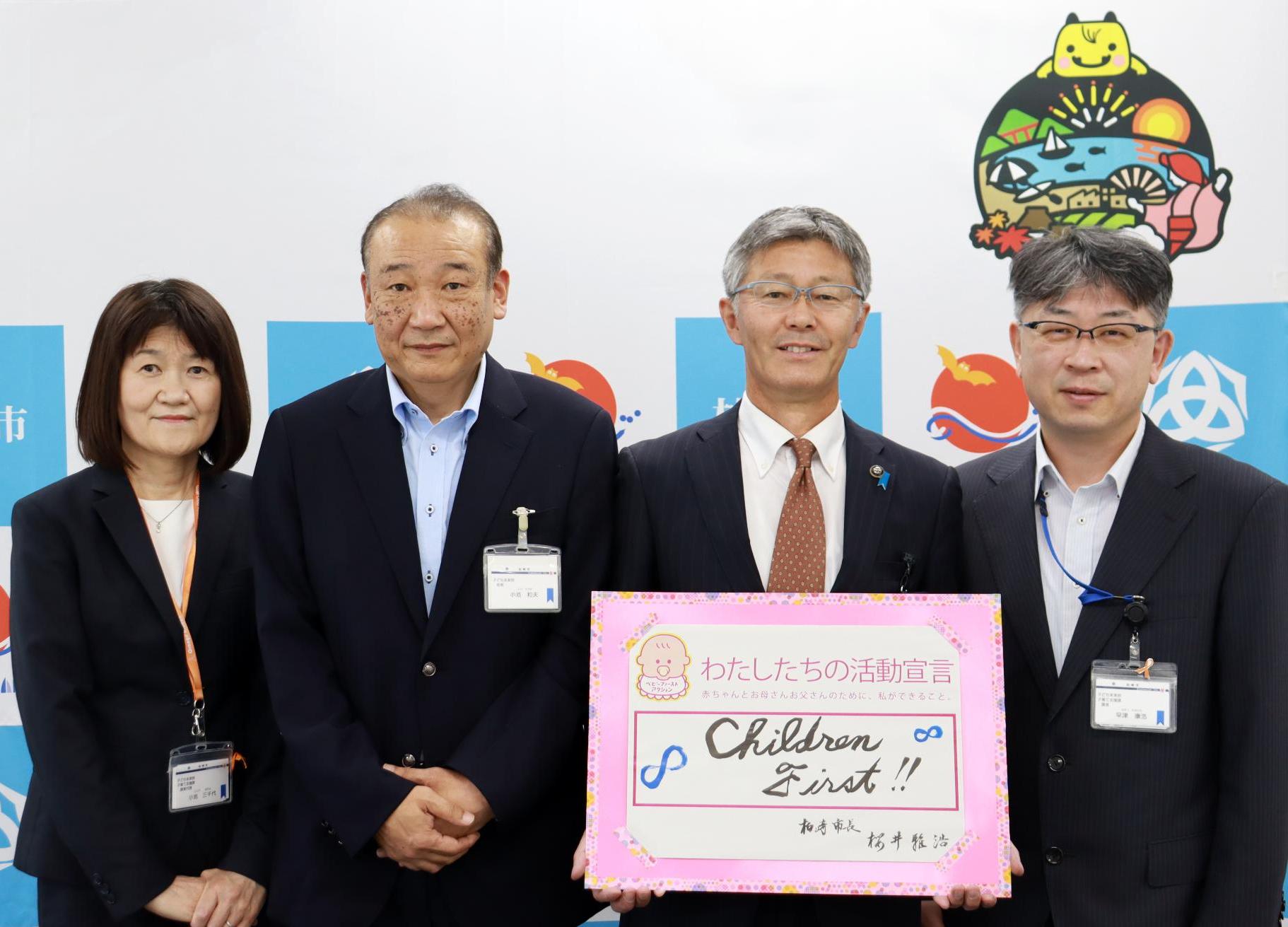 「私たちの活動宣言チルドレンファースト」の書類を持つ櫻井市長と職員3名