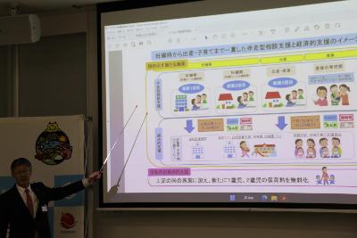 写真：市長がスクリーンを使いながら柏崎市の出産から子育てまでの経済的支援の説明をしています