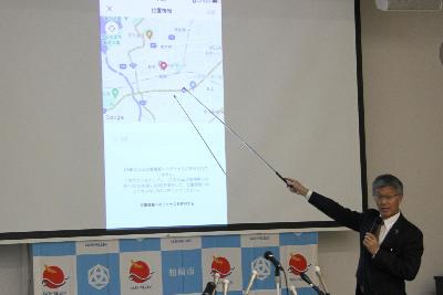 写真：市長がスクリーンに投影されたスマートフォンの画面を指しながら説明をしています