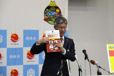 写真：市長が防災ガイドブック自然災害編を記者に見せながら説明しています。