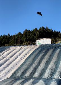 灰野さんがスノーボードで、大きなエアマットに向かって飛んでいます。
