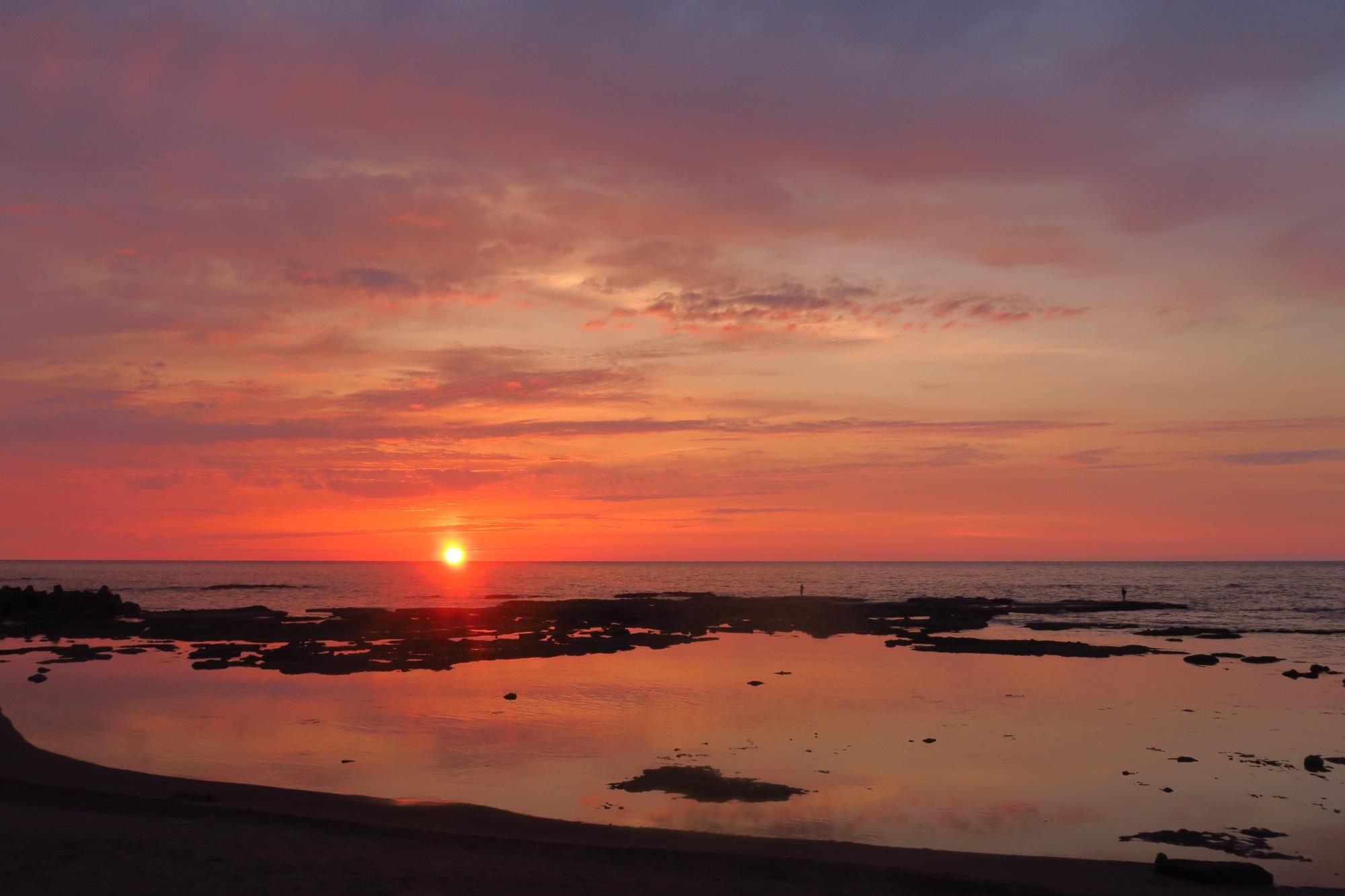 真っ赤な夕日が日本海に沈む写真。波が穏やかで海面には夕日に染まった雲が映っています。