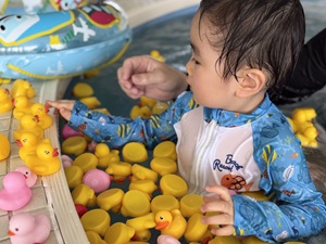 黄色いアヒルのおもちゃがたくさん浮かぶプールで遊ぶ子どもの写真