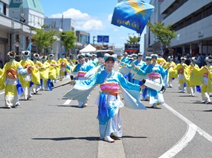 青と黄色の衣装で列になって演舞する参加者の写真