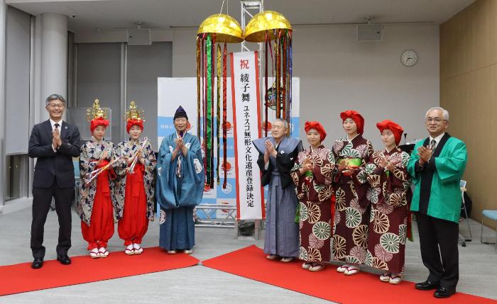 写真：市長と保存振興会会長、両座元の座頭・踊り手たちが、ユネスコ無形文化遺産の登録決定を受け、くす玉を割って祝っているところ