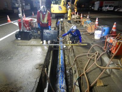 写真：夜間用の照明をつけながら、道路に水道管を敷設している作業員