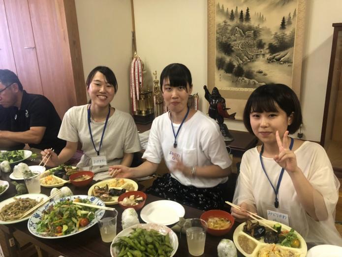 矢田集落にきた女性インターン生3人が食卓で地域の方が持ち寄ったご馳走をいただいている写真