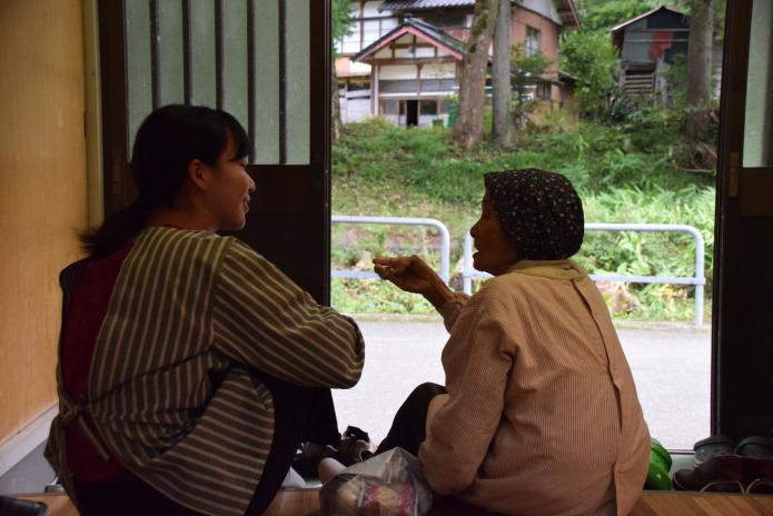 集落のおばあちゃんとインターン生が玄関に座り、話しをしている写真