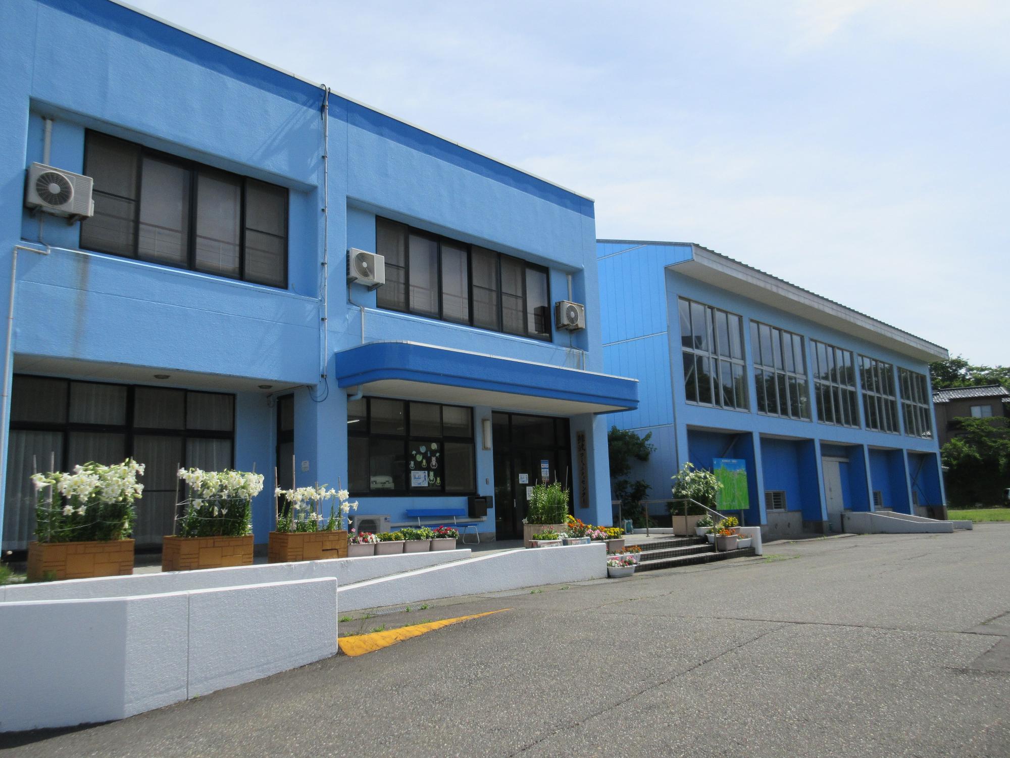 写真：鯨波コミセンの外観。手前に事務室や会議室のある本館、奥に体育館があります。外壁は海の色のように青一色で塗られています