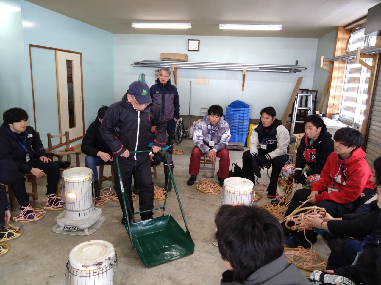 写真：小屋の中で地域住民からスノーダンプの使い方を教わるメンバー