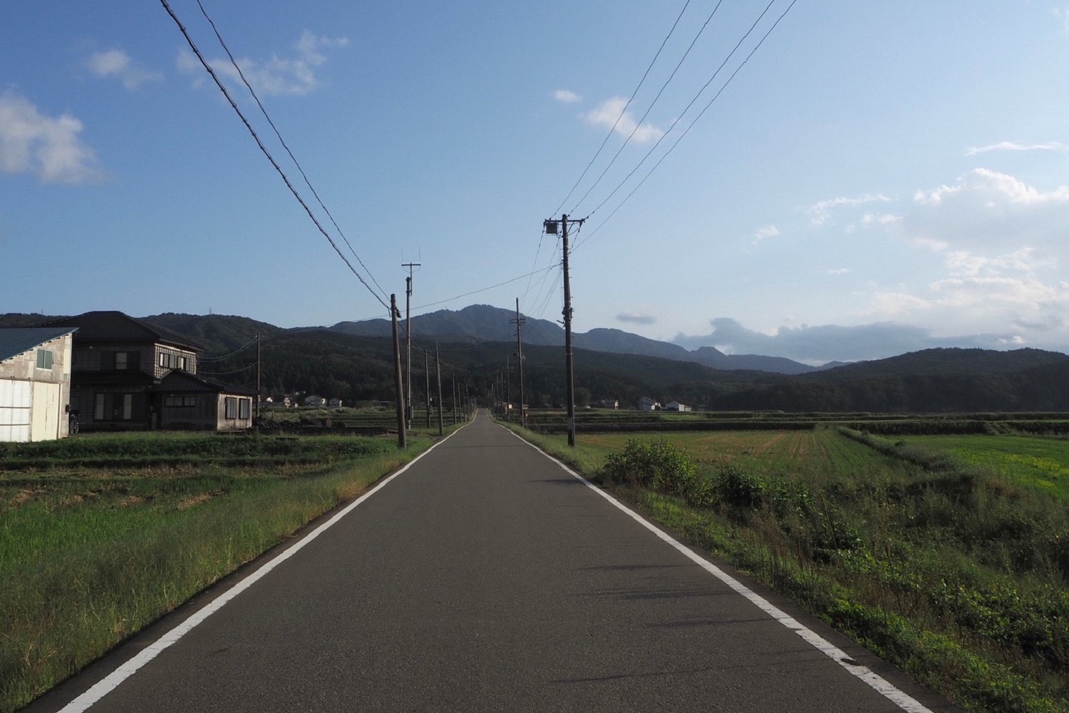 写真：別又地域の風景。直線道路の先には黒姫山がそびえ、道路の両側には田んぼが広がっています