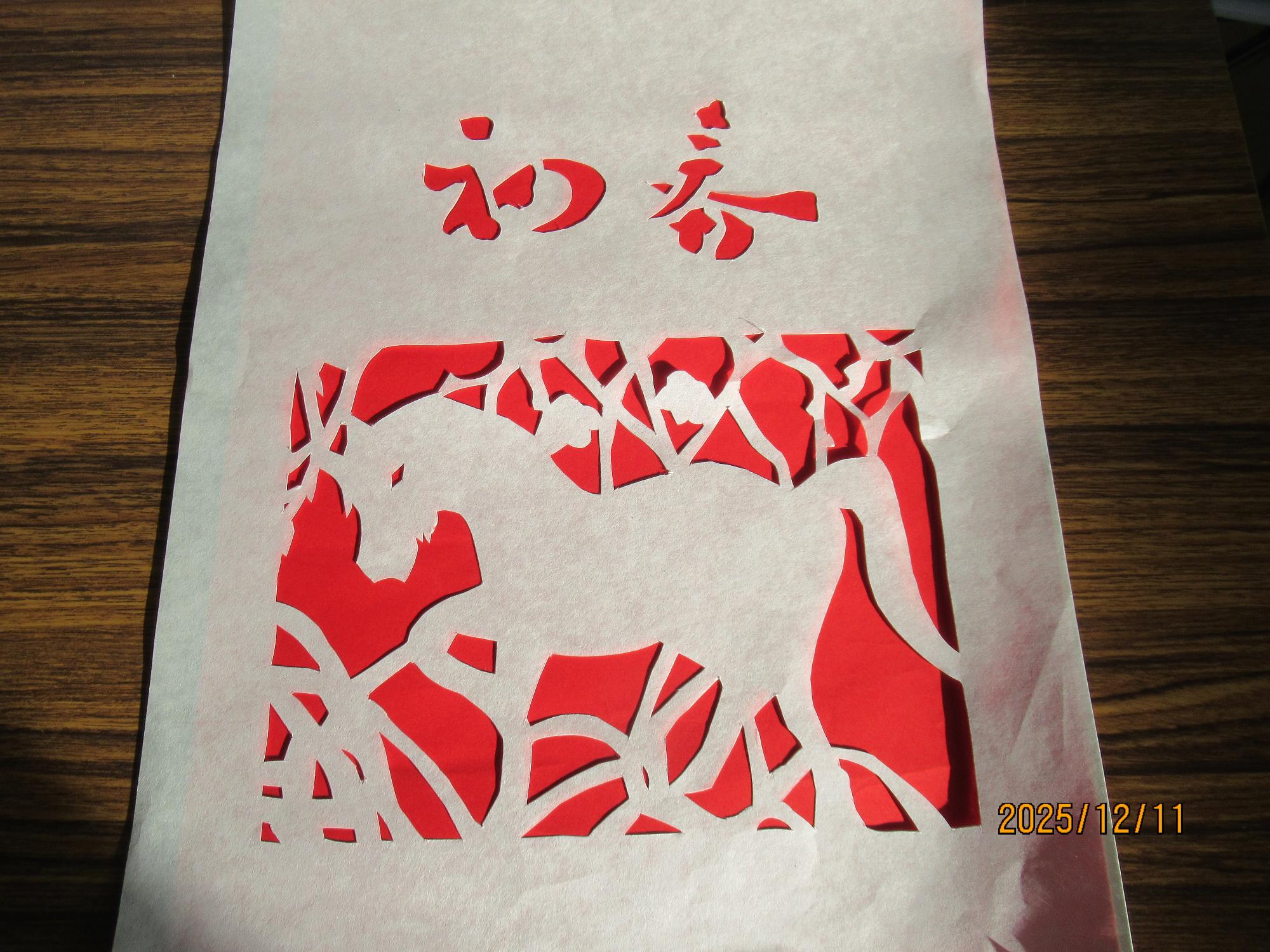 写真：赤い紙の上に、完成したはかま紙を重ねています。「初春」という文字と馬の絵柄が切り出されています