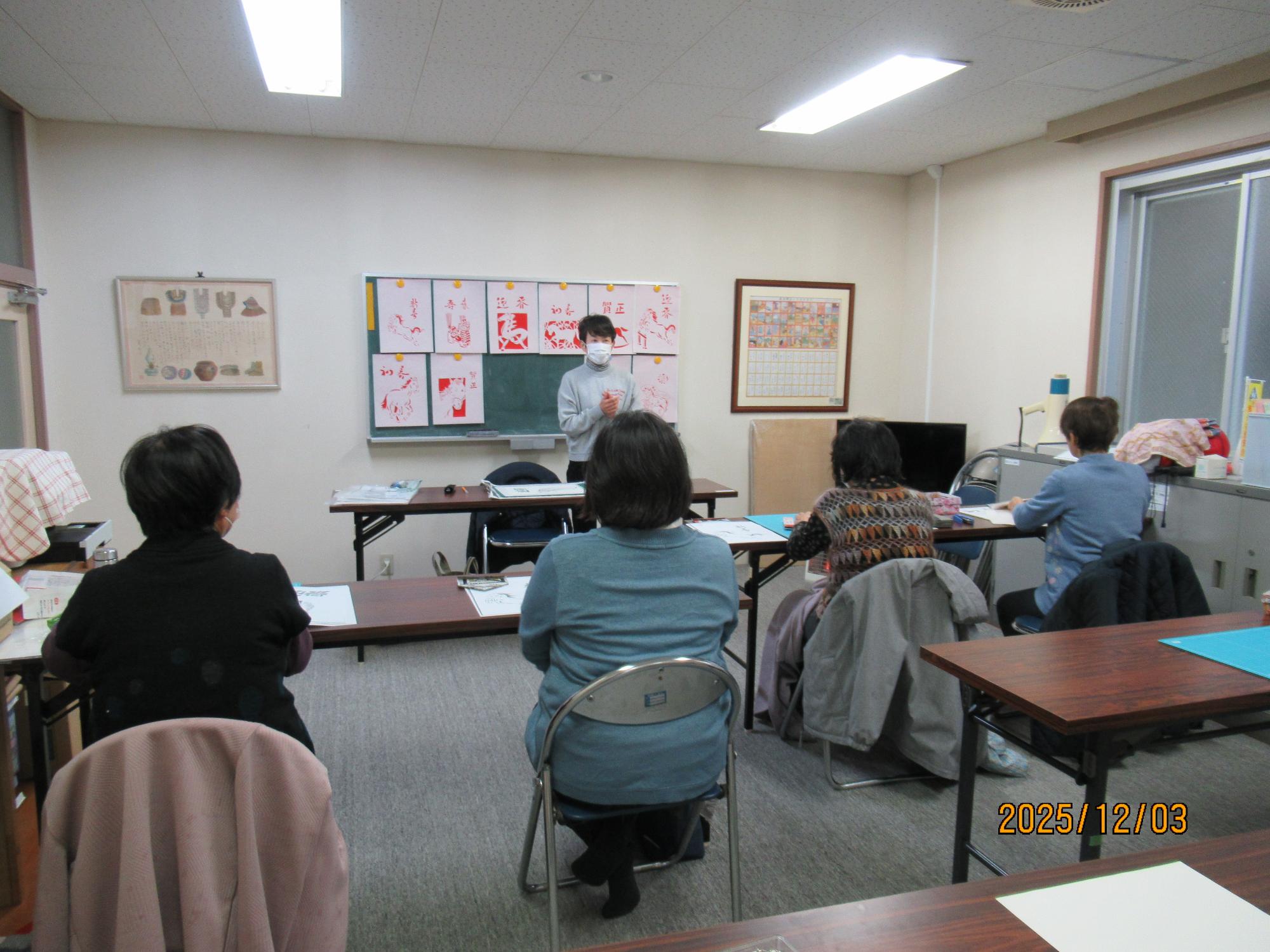 写真：はかま紙について説明している講師とその説明を真剣に聞く受講者