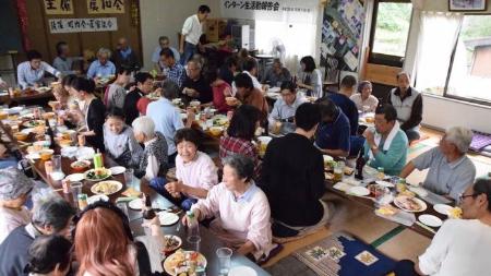 岩之入集落の収穫祭で集会場に集まった参加者が食事をしている写真