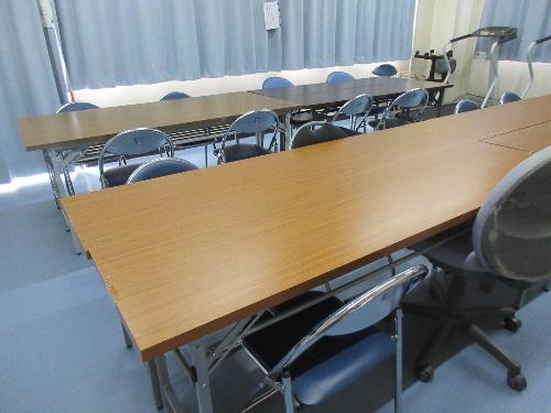 2人掛けの机が並んでいる研修室。奥にはトレーニングマシーンが数台あります