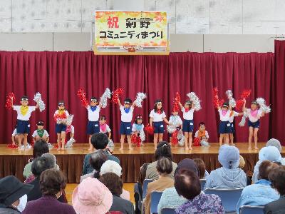 写真：剣野コミセンのステージいっぱいに子どもたちが並び、両手を挙げて演技している様子