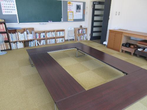 カーペット敷きの図書室。中央に座卓があり、壁側に黒板と図書が並んでいます