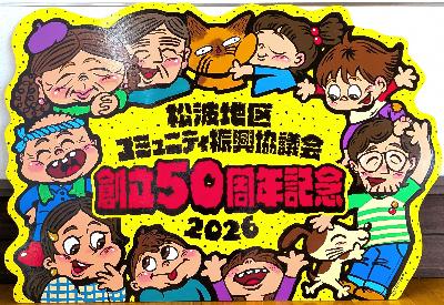 写真：創立50周年の記念のシンボルマーク看板。「松波地区コミュニティ振興協議会創立50周年記念 2026」の文字を中心に、その周囲に笑顔の老若男女・ペットのイラストが描かれています
