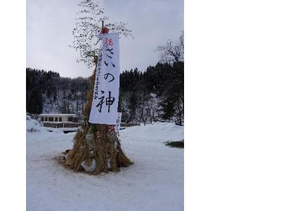 写真：長い竹を芯にして、周囲に稲わらを高く立てかけて作る主神。てっぺんから「さいの神」と書かれた白い紙が垂れています。